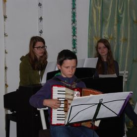 Junge spielt Akkordion, zwei Mädchen am Klavier